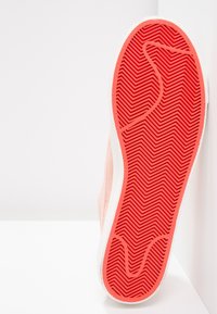 Rosa sneaker med en texturerad gummisula som visar ett fiskbensmönster. Ovandelen är mjuk, i en ljus färg med vita accenter.