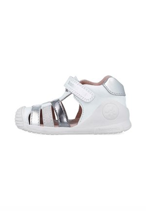 Sandalia infantil blanca y plateada, con un diseño abierto, correa de gancho y bucle, y suela de goma texturizada. Marca Biomecanics en el lateral.