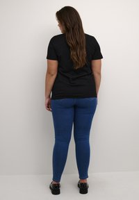 Svart kortärmad t-shirt i kombination med blå skinny jeans. Modellen står med långt brunt hår och bär svarta skor med tjock sula.