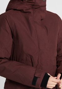 Körsbärsfärgad jacka med huva, med en slät tygtextur, justerbara ärmslut med kardborre och minimalistiska design detaljer.