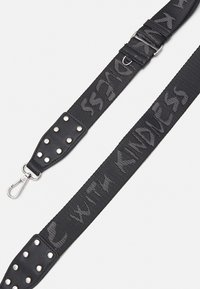Sangle en tissu noire réglable avec clip métallique et extrémités en cuir clouté, embossée du texte "AVEC BIENVEILLANCE".