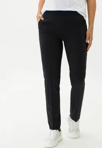 Zwarte fitted broek met een soepele textuur, elastische tailleband, zijzakken en subtiele plooien, gecombineerd met witte sneakers.
