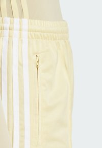 Lichtgele sportbroek met een gestructureerde afwerking, voorzien van drie witte strepen aan de zijkant en een ritszak. Inclusief elastische tailleband.