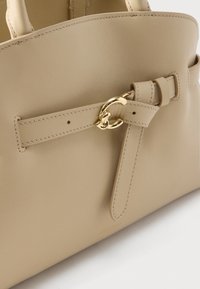 Μπεζ δερμάτινη τσάντα χειρός με λεπτομέρειες ραμμένης λουρίδας και αγκράφα σε χρυσό τόνο, που παρουσιάζει λεία υφή και μινιμαλιστικό σχεδιασμό.