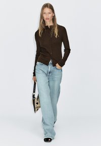 Brown ribbed cardigan with buttons, paired with light blue wide-leg jeans. Black open-toe sandals and a patterned handbag complete the look.