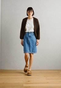 Brown knitted cardigan over a white t-shirt, blue denim skirt, and brown platform sandals. Smooth texture and casual fit.