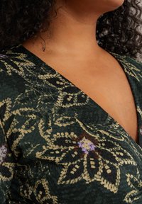 Material textil cu model floral verde, cu accente bej, mov și roșu. Prezintă un decolteu adânc în V și o suprafață texturată.