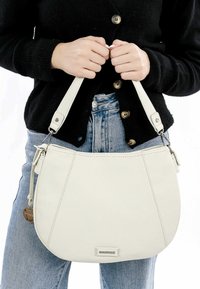Cream leather shoulder bag with a curved shape, featuring a short strap and a decorative charm. Textured surface with minimal hardware accents.