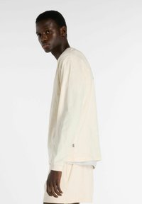 Romantische crème lange mouwen shirt van zacht materiaal, met een ontspannen pasvorm en subtiele logo-details. Combi met bijpassende crème shorts.
