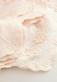 Broderad nude färgad tyg med texturerade blommönster, vågiga kanter och upphöjda detaljer; mjuk utseende och delikat hantverk.