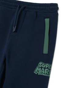 Donkerblauwe joggers met groene ritsdetails en het "Super Mario" logo dichtbij de zak, met een elastische tailleband met trekkoord.