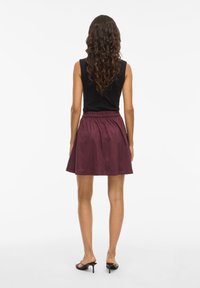 Un haut noir sans manches associé à une jupe bordeaux avec une taille élastique froncée, tombant jusqu'à mi-cuisse, d'une texture lisse.