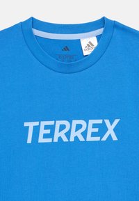 Μπλε βαμβακερό μπλουζάκι με στρογγυλή λαιμόκοψη, απαλό ύφασμα και τη λέξη "TERREX" τυπωμένη με μεγάλα λευκά γράμματα μπροστά.