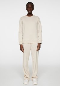 Beige sweatshirt en broek set, gemaakt van katoen, ronde hals, lange mouwen, ontspannen pasvorm, strakke lijnen, subtiele logodetail, gecombineerd met witte sneakers.