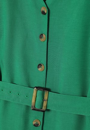 Groene jurk van een gestructureerde stof, met grote ronde knopen en een bijpassende riem met een vierkante gesp. Accentueert met stikseldetails.