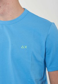 T-shirt blu a maniche corte realizzato in tessuto testurizzato, con un piccolo logo geometrico giallo sulla parte sinistra del petto. Collo rotondo a giro.