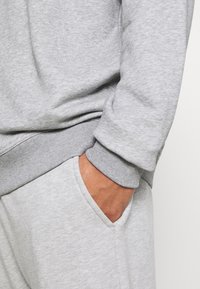 Felpa grigia con polsino a costine, dotata di tasca laterale sui pantaloni grigi abbinati. Tessuto morbido con finitura goffrata.