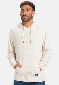 Pullover sweatshirt i lys creme med vandrette striber, frontlomme, justerbar snor og mærkat på den nederste søm.