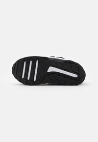 Semelle de chaussure de sport noire avec caoutchouc texturé pour une meilleure traction, dotée d'accents blancs et d'un design incurvé, améliorant l'adhérence et la flexibilité.