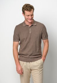 Brun kortärmad polo skjorta med en ribbad krage och treknapps-placket, tillsammans med ljusbeige byxor. Strukturerad stickad tyg.