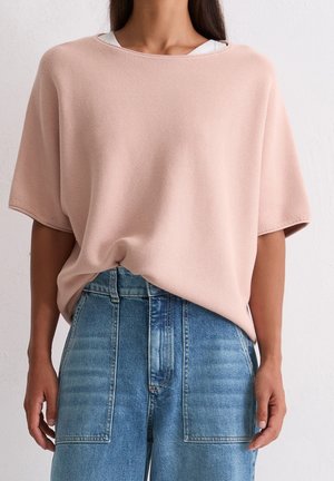 Personne portant un haut ample à manches courtes rose clair rentré dans un jean bleu taille haute avec de grandes poches avant.