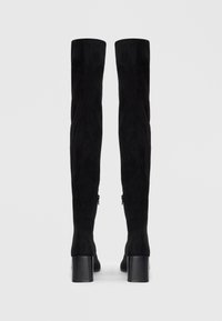 Svarta överknee-boots i mocka med en texturerad yta, utrustade med klack och blixtlås på utsidan.