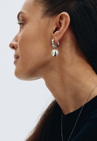 Metāla auskari ir aprīkoti ar mirdzošu pērļu pilienu ar melnu svītru, izceļoties ar pulētu sudraba apdari un elegantu dizainu.