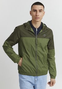 Green lightweight jacket with a hood, featuring a zip front, elastic cuffs, and tonal color blocking. The fabric appears smooth and water-resistant.