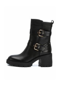 Bota de tobillo de cuero negro con dos correas de hebilla doradas, tacón grueso, suela texturizada y tirador lateral; presenta mínimos remaches decorativos.