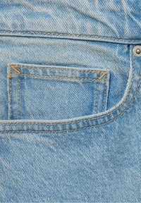 Vaaleansininen denimmateriaali, jossa on takatasku oranssilla tikkauksella, metallipiikkitaskun yksityiskohta ja hieman kulunut tekstuuri.