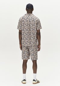 Short-sleeve button-up shirt and shorts in light beige with a blue and pink abstract pattern. Finished with a black cap and sneakers.