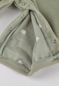 Light green baby bodysuit hem with snap buttons, showing soft fabric interior with small white crown patterns.
