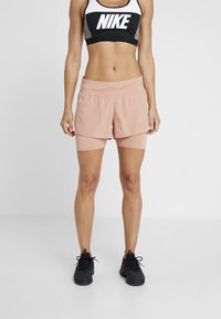 Sportowy biustonosz Nike w czerni i bieli z wycięciem na plecach typu racerback, połączony z brzoskwiniowymi szortami sportowymi o warstwowym kroju i perforowanych detalach.