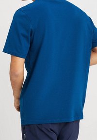 Tričko s krátkým rukávem a kulatým výstřihem v jednobarevné modro-zelené barvě z bavlny, s hladkým povrchem a uvolněným střihem, rovný lem a bez viditelných grafik.