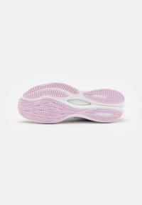 Semelle d'une chaussure de sport blanche et rose, présentant des motifs de relief et le logo "PUMAGRIP" sur fond blanc.
