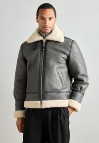 Γκρίζα δερμάτινη μπουφάν με γούνα, με απαλό κρεμ χρώμα στους γιακά και τους καφέ, με μπροστινό φερμουάρ και πλαϊνές τσέπες. Καθαρός, δομημένος σχεδιασμός.