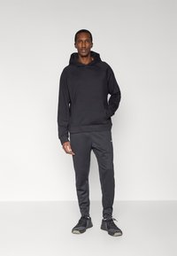 Sudadera negra con capucha y bolsillo delantero, combinada con pantalones jogger gris oscuro. Zapatillas deportivas negras con detalles texturizados.