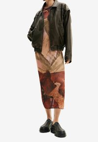 Brown leather bomber jacket over a flowing midi dress with abstract earthy tones. Black chunky shoes complete the outfit.