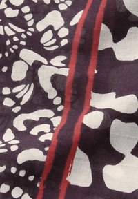 Écharpe en coton avec un fond violet foncé, des formes abstraites blanches et une large bande rouge, créant un design texturé et à motifs.