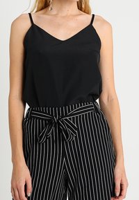 Schwarzes Satin-Camisole mit dünnen Trägern, kombiniert mit schwarz-weiß gestreiften, hochgeschnittenen Hosen mit einem Frontknoten-Detail.