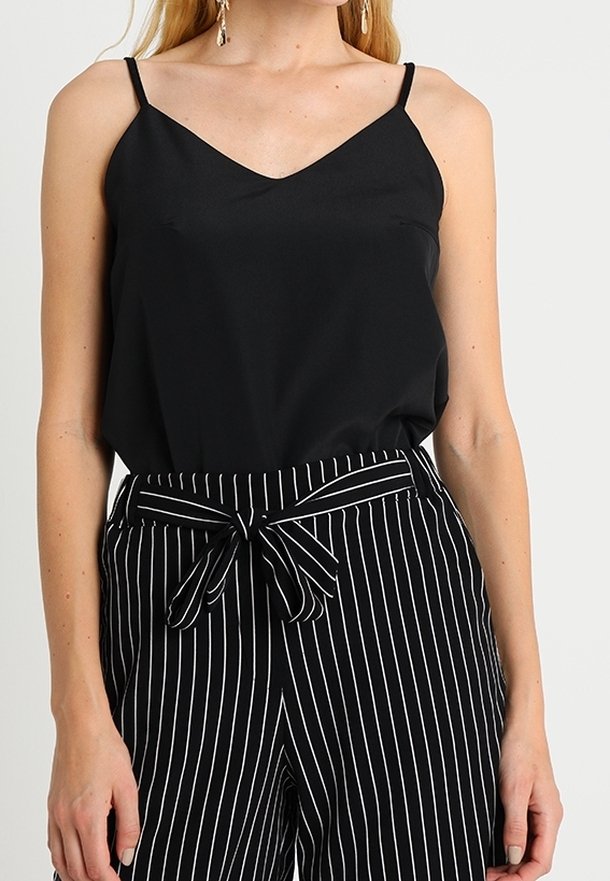 Schwarzes Satin-Camisole mit dünnen Trägern, kombiniert mit schwarz-weiß gestreiften, hochgeschnittenen Hosen mit einem Frontknoten-Detail.