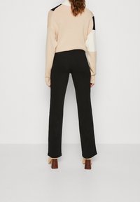 Cremfarbener und schwarzer Blockfarbenpullover mit lockerer Passform, kombiniert mit schwarzen Ripp-Hosen und beigen Blockabsatzschuhen. Einfaches Design, minimale Details.