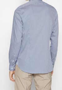 Skjorta med knappar i blå och vit rutig mönster; långa ärmar med knappmanchetter; rundad fåll; lättviktsmaterial med en slät textur.