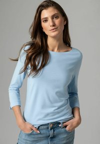 Hellblaues Langarmoberteil mit rundem Ausschnitt, glatter Textur und figurbetonter Passform, getragen mit Jeans. Einfacher und lässiger Stil.
