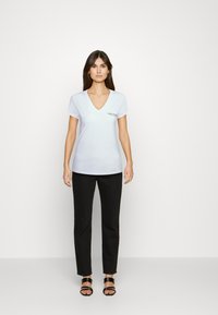 White v-neck t-shirt with short sleeves and a fitted design, paired with black slim-fit trousers and black strappy sandals.
