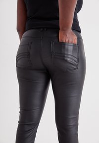 Black faux leather pants with a tight fit, featuring stitched pocket details and a smooth texture. High-waisted design and decorative seams.