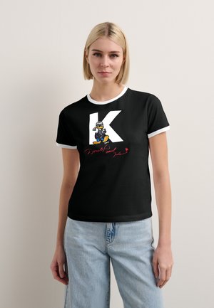 Camiseta de manga corta negra con ribete blanco que presenta una gran 'K' blanca y un gráfico de un personaje de dibujos animados en una patineta.