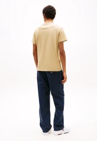 Camiseta de algodón beige con mangas cortas, cuello redondo y un ajuste relajado. Combinada con pantalones cargo azul marino que cuentan con múltiples bolsillos y una textura suave.