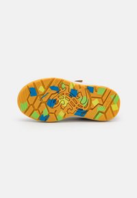 Semelle de chaussure en caoutchouc multicolore avec un motif en nid d'abeille. Présente un fond jaune avec des accents bleu, vert et noir et un design de grenouille.