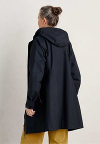 Cappotto impermeabile nero con cappuccio, maniche lunghe e vestibilità rilassata. Presenta una cerniera e dettagli con coulisse in vita e sulle maniche.